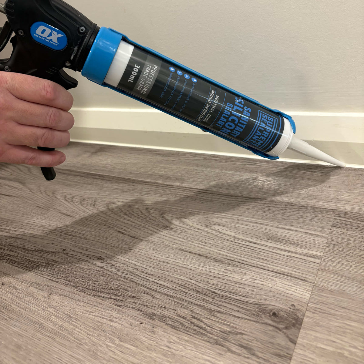 Applying Supreme Sealants sanitary silicone along a skirting board with a caulking gun